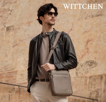 Mann mit Sonnenbrille und schwarzer Lederjacke trägt eine taupefarbene Umhängetasche und steht vor einer strukturierten Steinwand mit dem "WITTCHEN"-Logo darüber.