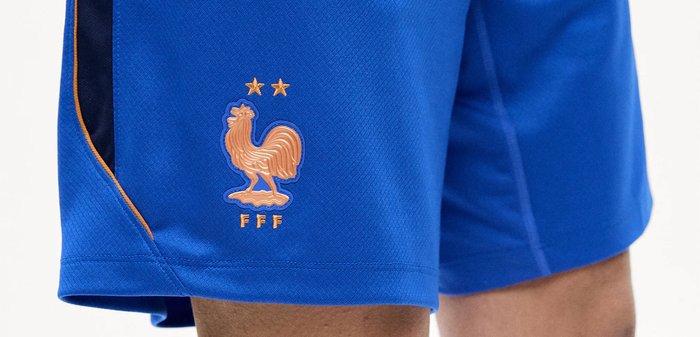 Μπλε αθλητικό σορτς με το λογότυπο της Γαλλικής Ποδοσφαιρικής Ομοσπονδίας και δύο αστέρια πάνω από ένα χάλκινο έμβλημα πετεινού.