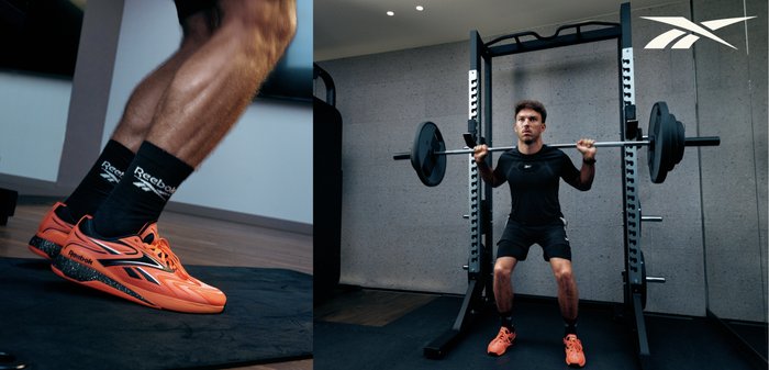 Mann trägt orangefarbene Reebok-Schuhe und schwarze Sportkleidung und macht Kniebeugen mit einer Langhantel in einem Fitnessstudio, die Gewichte stehen auf einer schwarzen Matte.