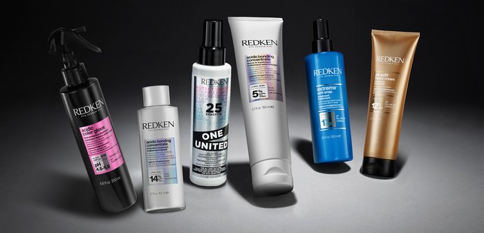 Sei prodotti per la cura dei capelli Redken: diverse forme e dimensioni, bottiglie di plastica in nero, bianco, blu e oro; etichette con dettagli e istruzioni sul prodotto.