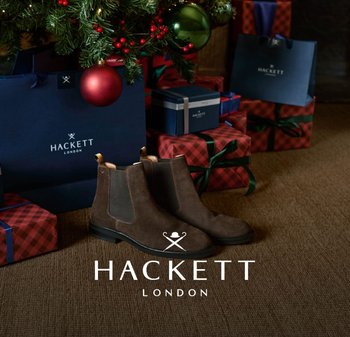 Brown suede Chelsea boots with elastic side panels, tan accents, and a sleek black rubber sole, placed near wrapped gifts under a tree.