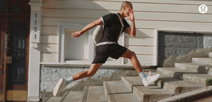 Atletische schoenen in het wit, zwarte shorts en een zwart shirt met een grijze rand; blauwe sokken zichtbaar terwijl de persoon de betonnen trappen afrent.
