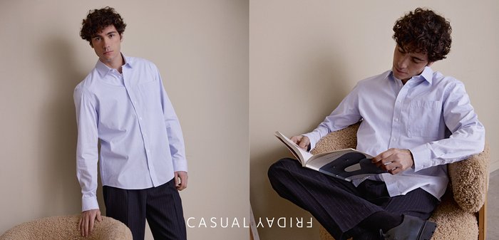 Hellblaues, gestreiftes Hemd mit Knöpfen und Brusttasche, kombiniert mit dunkler Nadelstreifenhose, sitzt in einem strukturierten beigen Sessel und liest ein Buch.