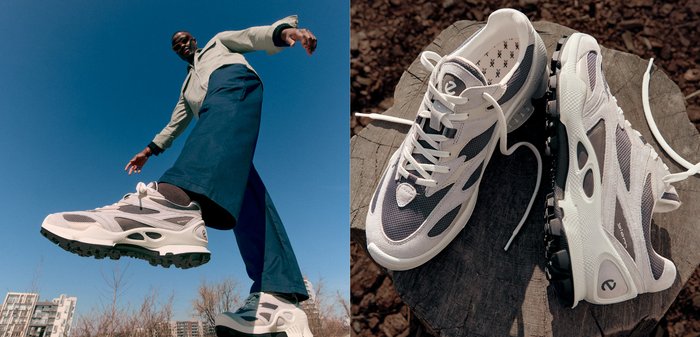 Witte en grijze sport schoenen met mesh overlays, een gewatteerde zool en een zwarte rubberen buitenzool. Gedetailleerd met veters en branding op de tong.