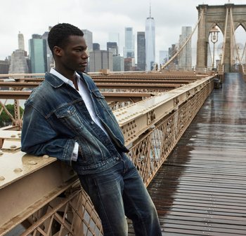 Denimjack met een vervaagde blauwe afwerking, gedragen over een wit shirt, gecombineerd met donkerblauwe jeans. Achtergrond toont een stedelijke skyline en brug.