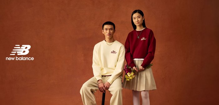Pull crème avec logo bordeaux et pantalon en velours côtelé beige portés par un homme. Femme en pull bordeaux et jupe plissée beige tenant des fleurs.