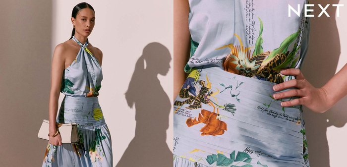 Femme portant une robe longue sans manches à col halter avec des motifs floraux et d’écriture, tenant une pochette beige et portant des sandales noires.