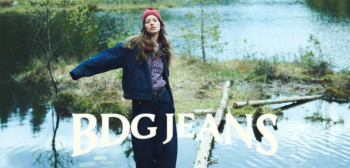 Outfit di jeans BDG con giacca in denim scuro e dalla vestibilità ampia e jeans larghi scuri. Abbinato a un berretto di lana rosso e una camicia a quadri sotto.