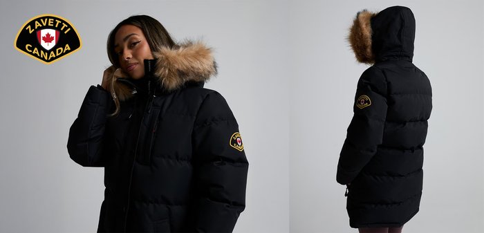 Vrouw met een zwarte Zavetti Canada winterjas met een met bont gevoerde capuchon, die de zijkant van haar hoofd aanraakt, tegen een effen grijze achtergrond.