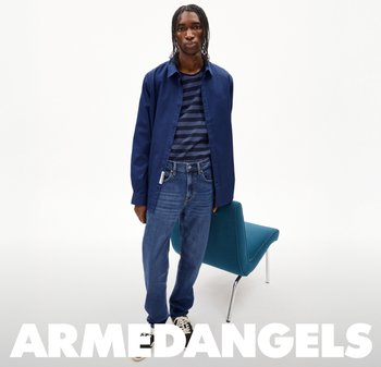 Navy-blaues Hemd über einem navy-blauen gestreiften T-Shirt, kombiniert mit hellblauen Jeans und schwarzen Sneakers, vor einem weißen Hintergrund.