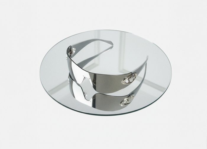 Fényes ezüst dizájnnal készült napszemüveg, ívelt forma, tükröződő lencsék és hangsúlyos fém részletek, kerek üveglapon bemutatva.