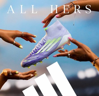 Botte de football violet clair avec des accents vert lime, un col haut style chaussette et une surface texturée, tenue entre deux mains. Logo de la marque visible.