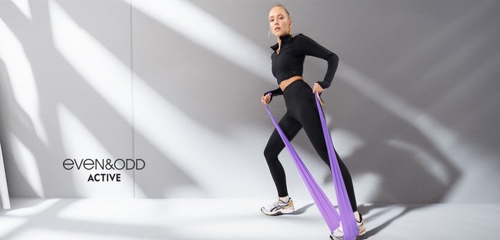 Zwarte sportieve crop top en hoge taille leggings met een gladde textuur. Paarse weerstandbanden in gebruik. Grijze textuur achtergrond.