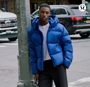 Blauwe pufferjas met capuchon, met een glanzende, doorgestikte textuur en zichtbare naden. Draagt over een wit shirt en gecombineerd met donkere broek.