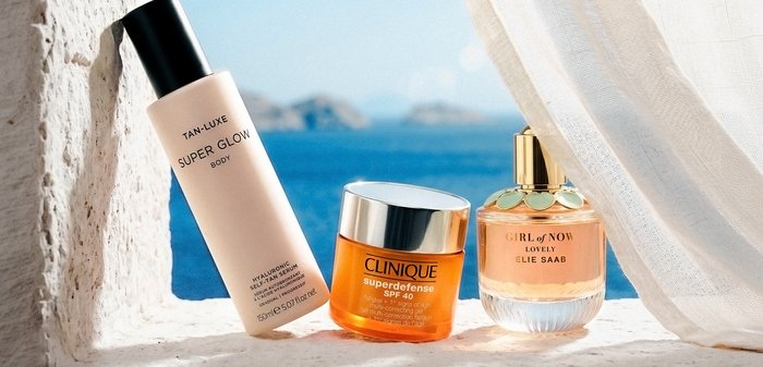 Trois produits de soin de la peau et de parfum sur un rebord blanc près d'une fenêtre avec vue sur la mer et un rideau transparent.