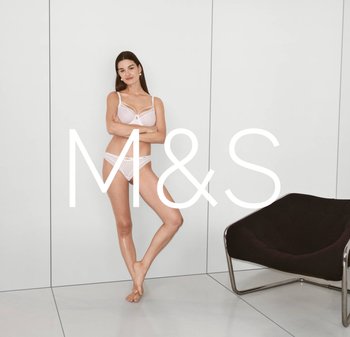 Ensemble de lingerie en dentelle blanche avec des panneaux en maille, comprenant un soutien-gorge doux et une culotte assortie. Le modèle se tient devant un mur clair, mettant en valeur l'ensemble.