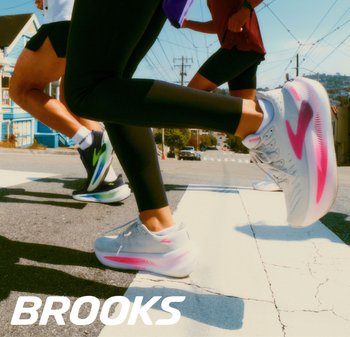 Lichtgrijze hardloopschoenen met roze accenten en een gestructureerd mesh bovenwerk, gecombineerd met zwarte leggings, terwijl hardlopers een straat oversteken.