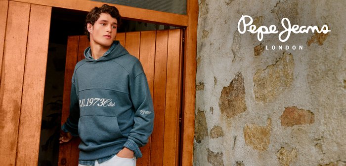 Felpa blu con cappuccio con testo stampato bianco, dotata di tasca a marsupio e vestibilità casual. Indossata con pantaloni chiari su sfondo di legno.