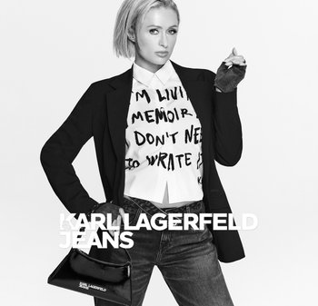 Black blazer over a white shirt with black text, dark jeans, and a small glossy black handbag. Simplistic monochrome styling.