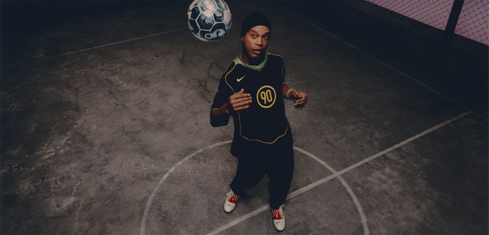 Maglia sportiva nera con accenti gialli, con il numero 90, abbinata a pantaloni neri. Un pallone da calcio fluttua sopra un giocatore in un contesto di campo.