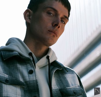 Grijze en witte geruite flanellen shirt met zwarte knopen over een lichtgrijze hoodie, met trekkoorden en subtiele textuurelementen.