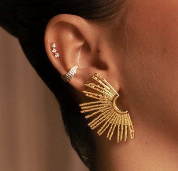 Orecchini in oro con un motivo a raggiera con raggi allungati. Sono visibili anche piccoli orecchini a lobo con diamanti nella parte superiore dell'orecchio.