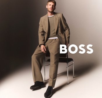 Ljusbrun dubbelknäppt kostym med matchande byxor och en grön tröja under. Svarta dress shoes, sittande mot en neutral bakgrund.
