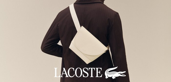 Personne portant une veste marron foncé avec un sac bandoulière blanc en travers du dos sur un fond neutre.