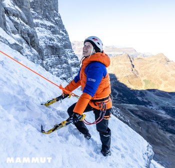 Orangene und blaue puffige Jacke mit strukturierter Oberfläche, Eispickel in der Hand, Klettern auf schneebedecktem Felsen, mit Sicherheitsausrüstung gesichert.