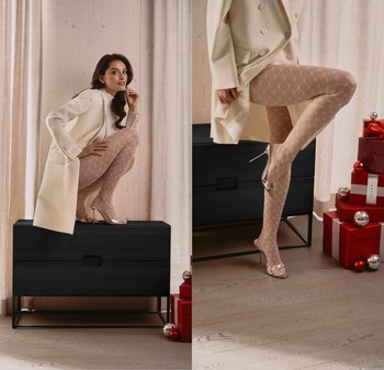 Beige gemusterte Strumpfhosen mit einem Wabenmuster, kombiniert mit silbernen High Heels und einem cremefarbenen, doppelt geknöpften Mantel, vor einem minimalistischen Hintergrund präsentiert.