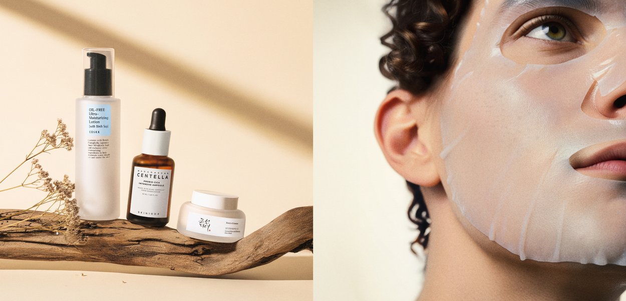 Hautpflegeprodukte auf Treibholz mit getrockneten Blumen daneben, Nahaufnahme einer Person, die eine durchsichtige Tuch-Gesichtsmaske aufträgt.