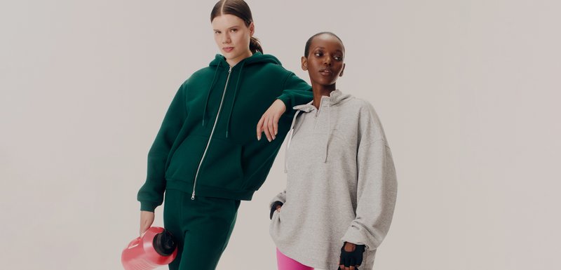 Πράσινη zip-up μπλούζα με τσέπες μπροστά, συνδυασμένη με αντίστοιχες φόρμες. Γκρίζα pullover μπλούζα με ψεύτικο λαιμό και ροζ κολάν. Κόκκινο μπουκάλι νερού.