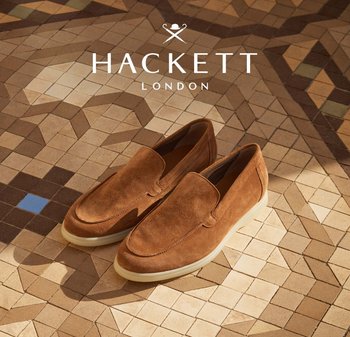 Zapatos de ante marrón tipo slip-on con suelas blancas colocados sobre un suelo de baldosas con diseño, con el logo de Hackett London arriba.
