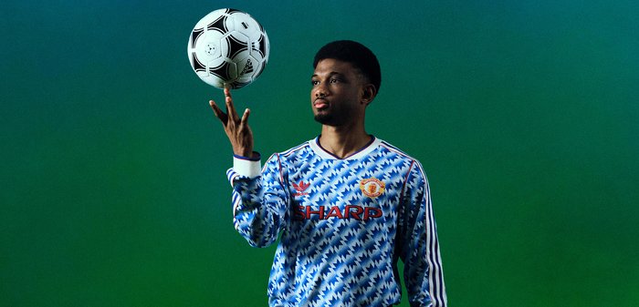 Kolm meest poseerivad rohelise-sinise gradiente taustal, kandes retro Manchester United jalgpalliriideid, üks hoiab jalgpallipalli, üks istub pingil.