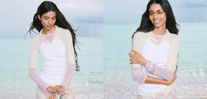 Jeune femme aux longs cheveux foncés portant des vêtements légers superposés près de la mer, regardant vers le bas à gauche et souriant les yeux fermés à droite.