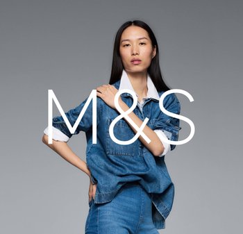 Chemise en denim avec un col blanc, dotée de poches avant et de manches retroussées, associée à un pantalon en denim. Le modèle pose devant un fond gris.