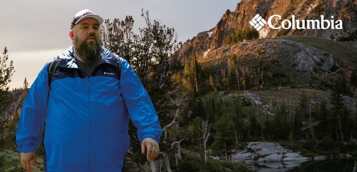 Blue waterproof jacket with black accents, lightweight material, zippered front, and elastic cuffs; worn with a backpack in a natural setting.