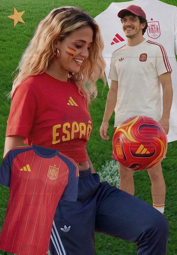Junge Frau und Mann lächeln, tragen spanische Fußballtrikots; Frau hat Gesichtsfarbe mit der Flagge; Mann hält einen roten Fußball auf einem grünen Rasenfeld.