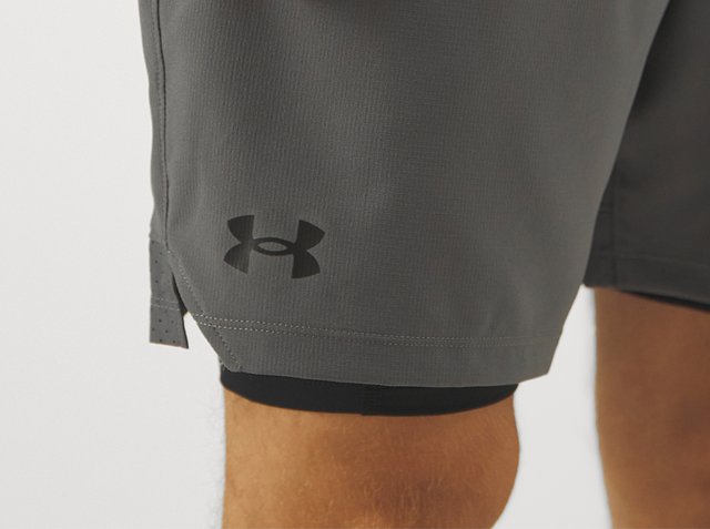 Grijze Under Armour short op de dij van een persoon met een zwart logo nabij de zoom en zwarte compressieshorts eronder.