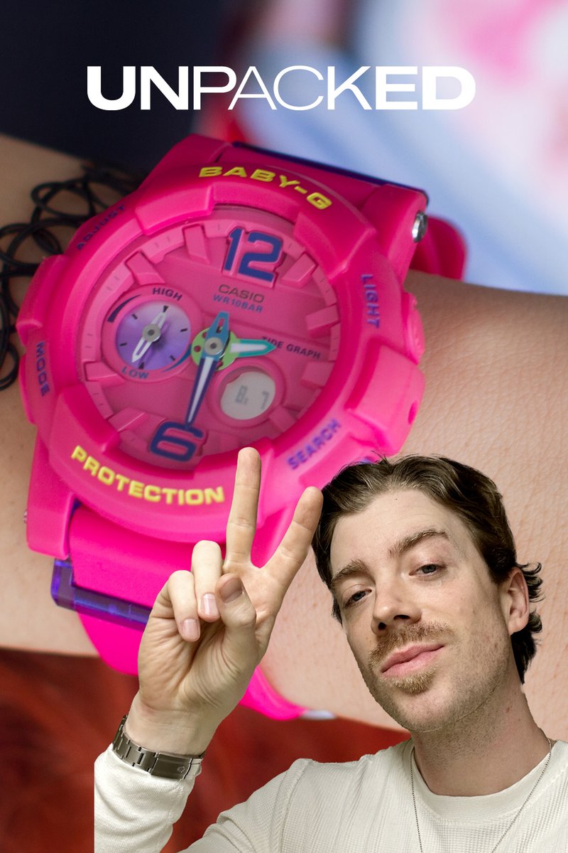 Osoba drží dvě prsty vedle vibrace růžových hodinek Casio Baby-G na svém zápěstí, které mají tučné číslice a barevný design.