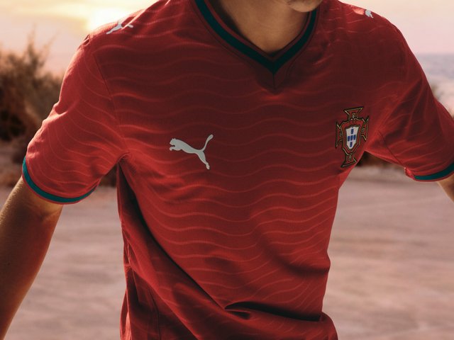 Rød Portugals fotballdrakt med subtil bølgetekstur, grønnkantet krage og ermer, Puma-logo og nasjonalt våpenskjold på brystet.