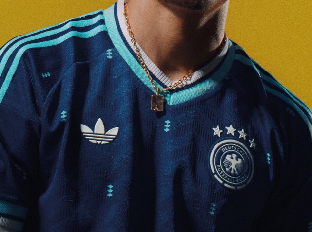 Persoon draagt een donkerblauw Duits voetbalshirt met lichtblauwe strepen en vier sterren boven het nationale embleem.