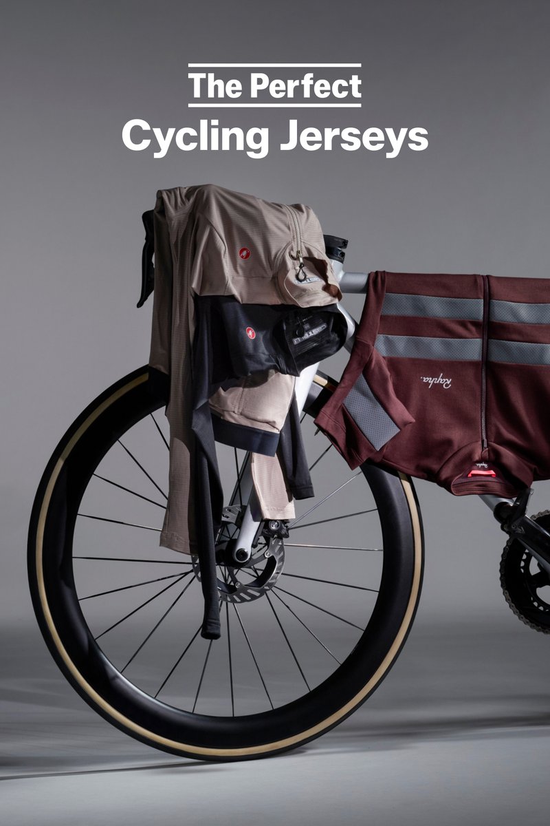 Fahrradtrikots und -shorts in Beige und Dunkelrot liegen über einem Fahrrad, das ein Rad mit dunklem Felgen und einem grauen Hintergrund hat.