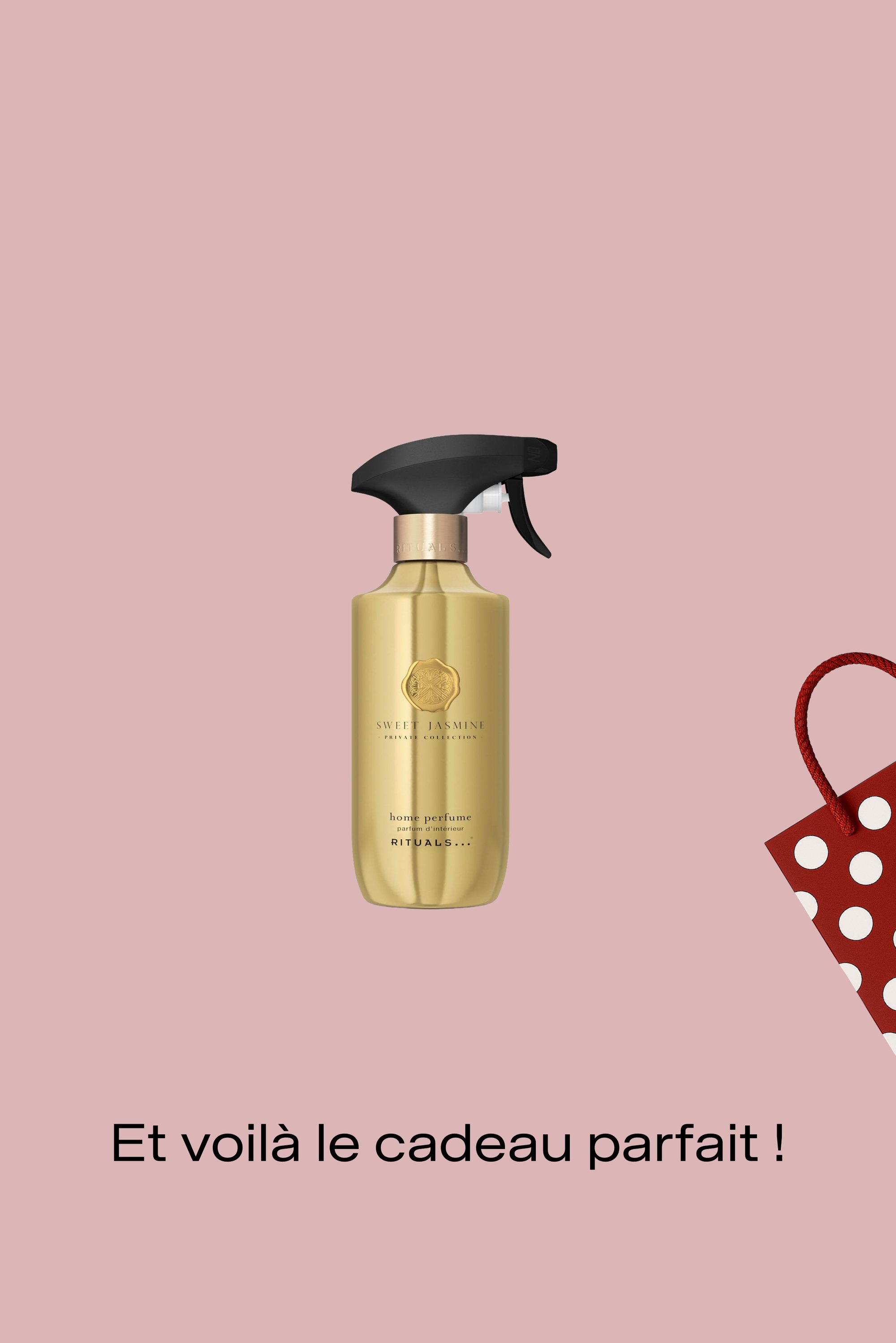 Bouteille vaporisateur dorée étiquetée Parfum d'intérieur Jasmin Doux par Rituals sur fond rose avec coin de sac cadeau à pois rouges, texte en français en dessous.