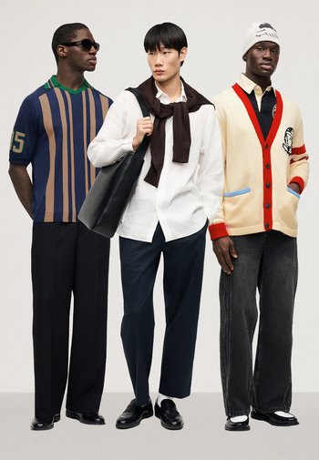 Three men standing wearing casual outfits: striped polo, white shirt with sweater, and cream cardigan with beanie, posing against a plain background.