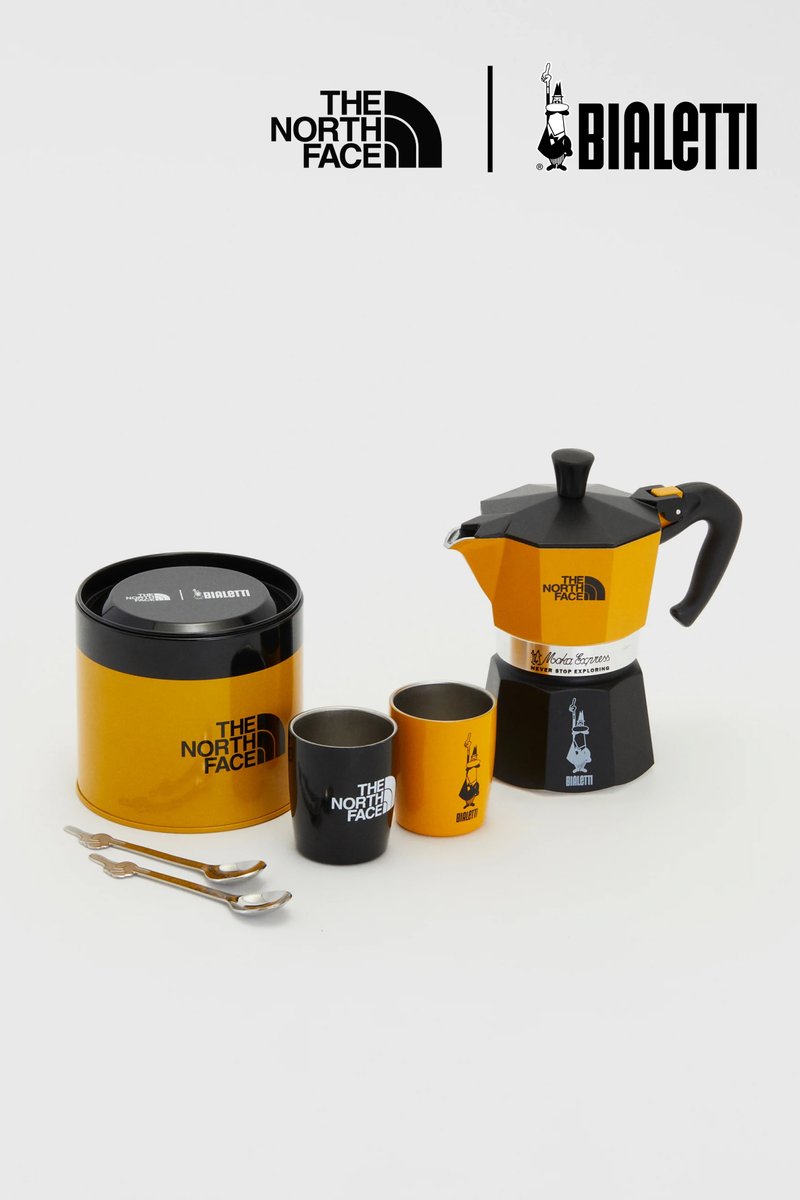 Moka pot set met een zwarte en oranje aluminium moka pot, twee kopjes (zwart en oranje), een blikken container en twee metalen lepels.