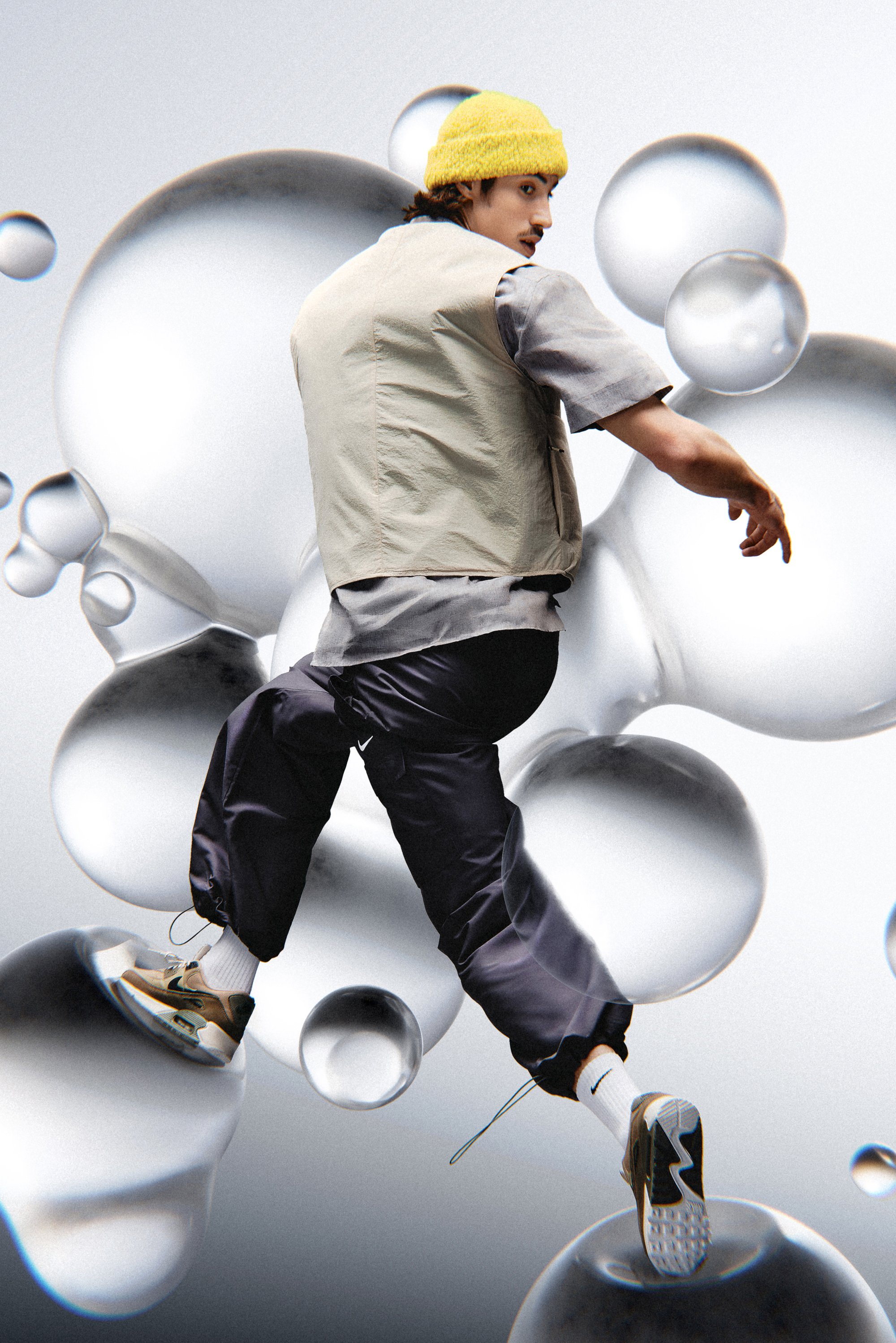 A person in a beige vest and yellow beanie strikes a dynamic pose on transparent bubbles against a light gray background.