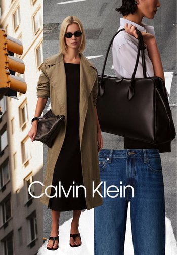 Blonde woman wearing sunglasses, beige trench coat, black dress, holding a black clutch, standing on urban street background with Calvin Klein logo.
