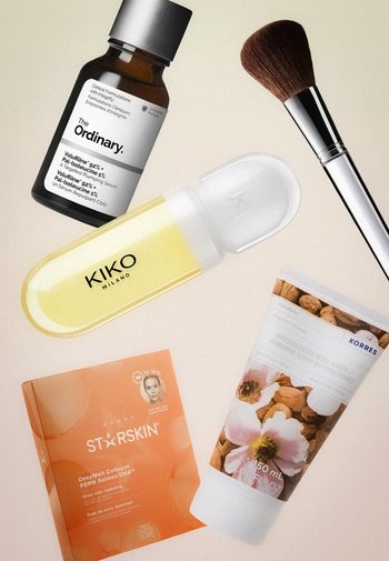 The Ordinary serumflesje, KIKO Milano gele huidverzorgingsfles, make-upkwast, Korres body scrub tube en oranje STARSKIN collageenmaskerdoos op een beige oppervlak.
