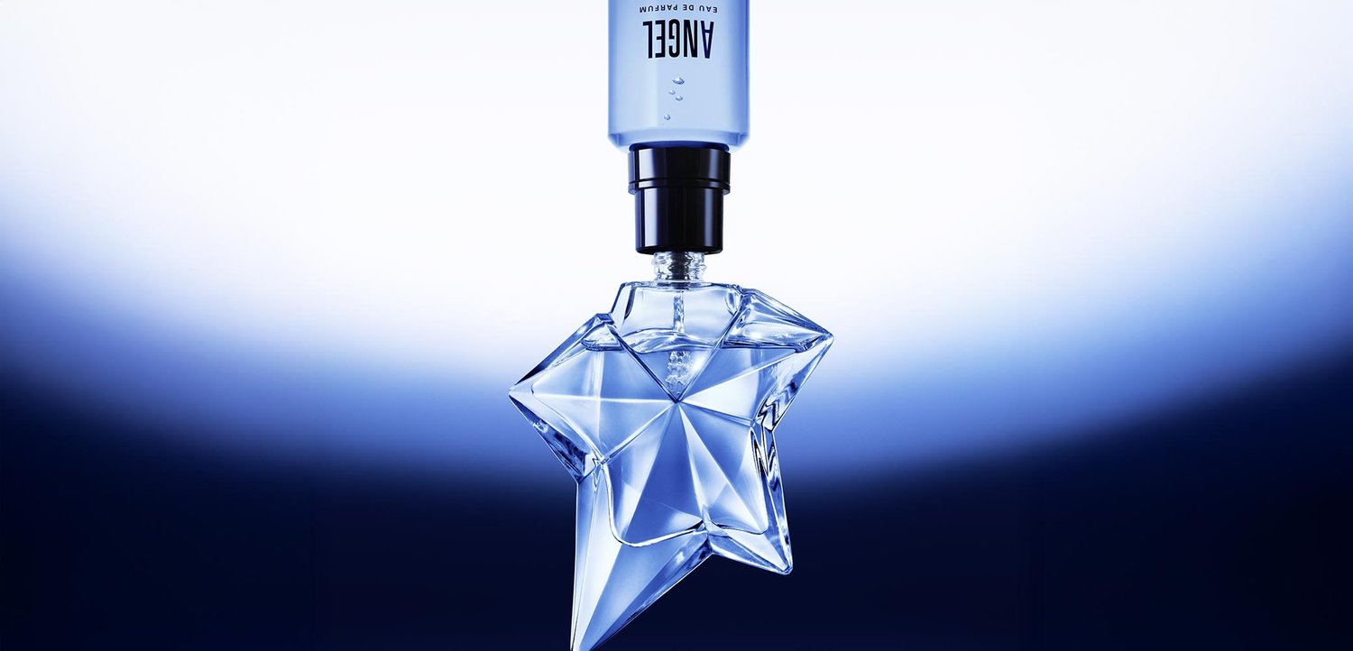 Blauer sternförmiger Parfümflakon mit facettiertem Oberflächen, silbernem Deckel und klarem Sprühkopf. Der Hintergrund verblasst von hellblau zu dunkelblau.